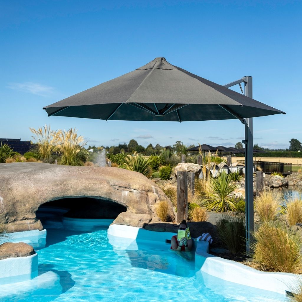 Shadowspec Serenity umbrella at a resort poolside with blue sky and plants