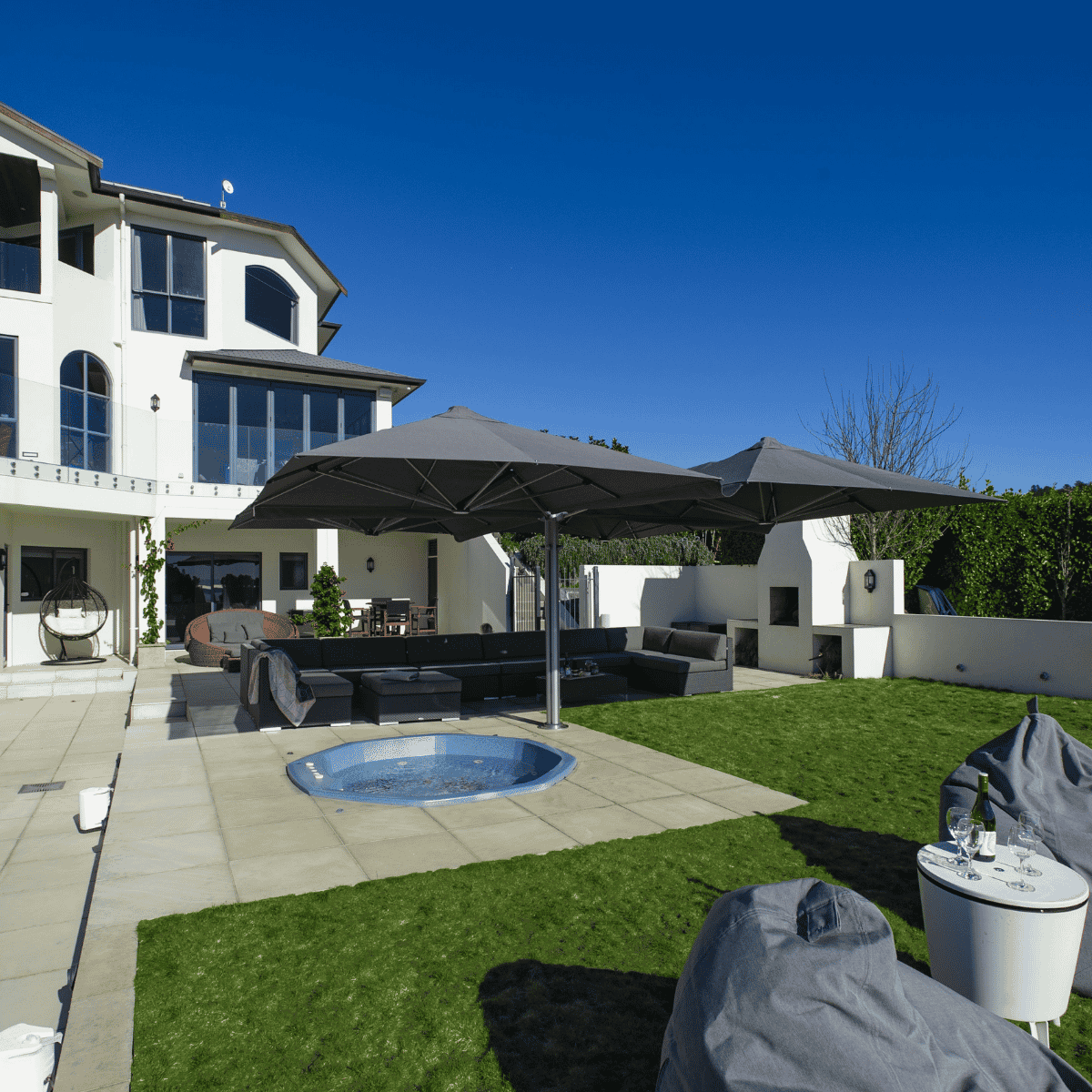 Outdoor patio area with lounge furniture, Shadowspec Unity Quattro umbrella, and a pool in front of a house.