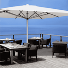 Shadowspec Commercial Center Pole Umbrella with white canopy on a restaurant deck overlooking the ocean